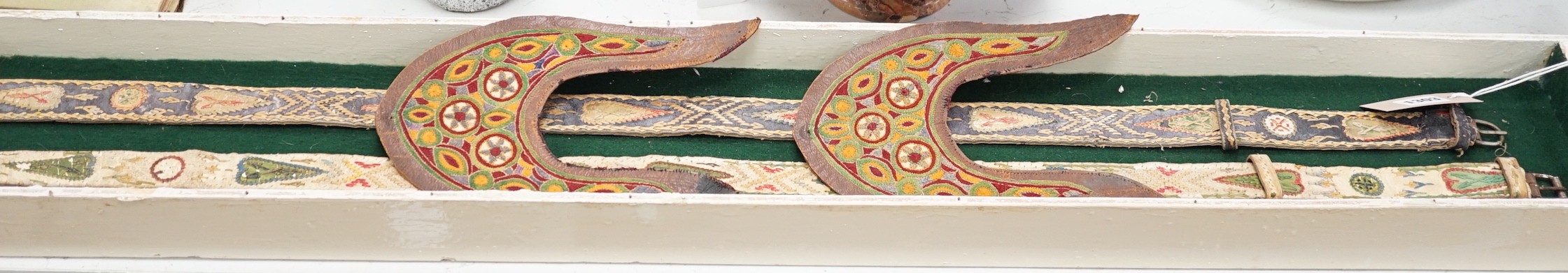 A two framed native American Indian ornately woven and embroidered leather belts and a pair of leather embroidered slipper fronts, longest belt 103cms